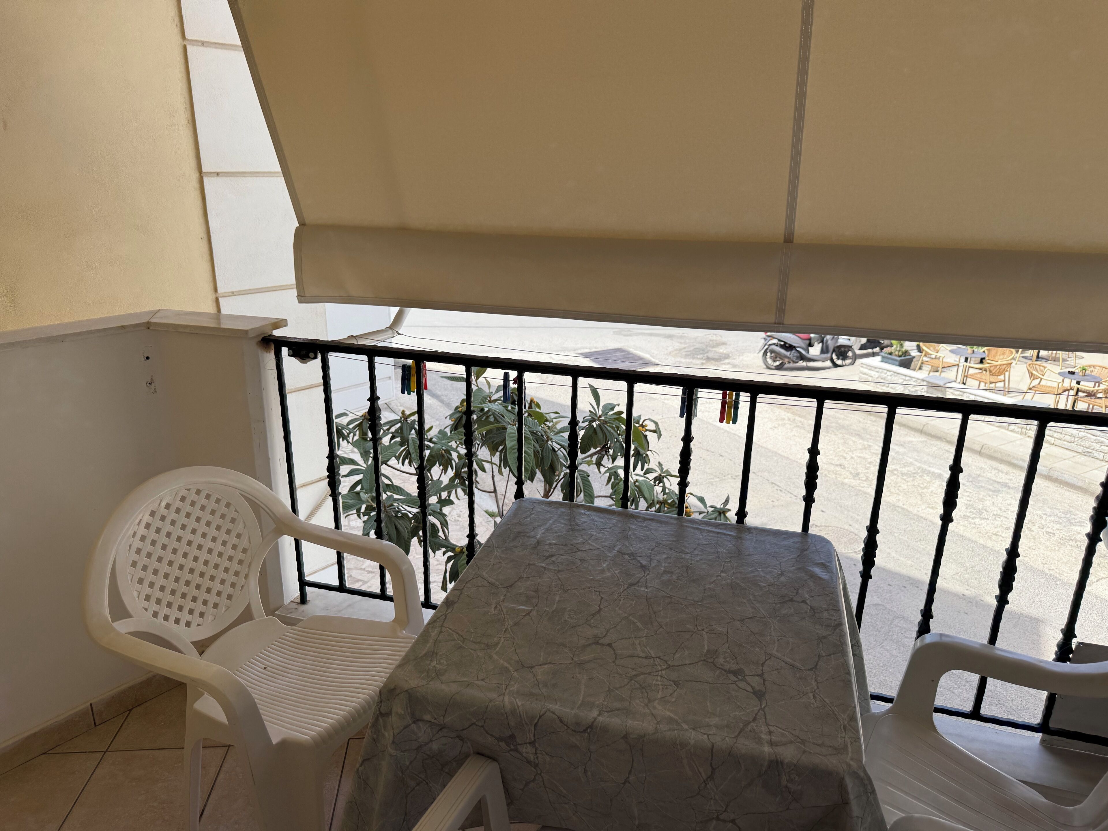 Een balkon met een tafel, twee stoelen, uitzicht op de straat en een plant.