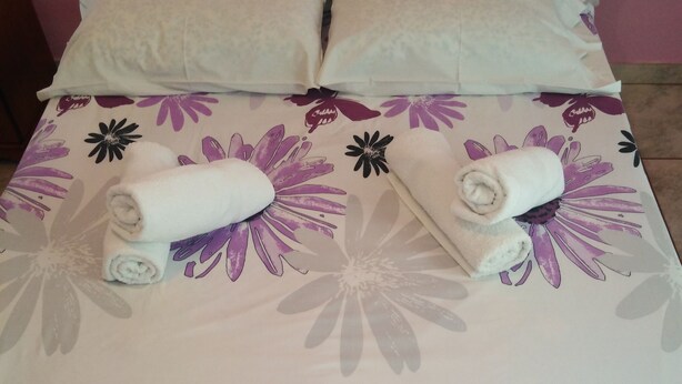 A bed with a floral bedspread, two rolled towels, and two pillows. - New Panorama Studios (ELECTRIC CAR CHARGING STATION) (North Kynouria)