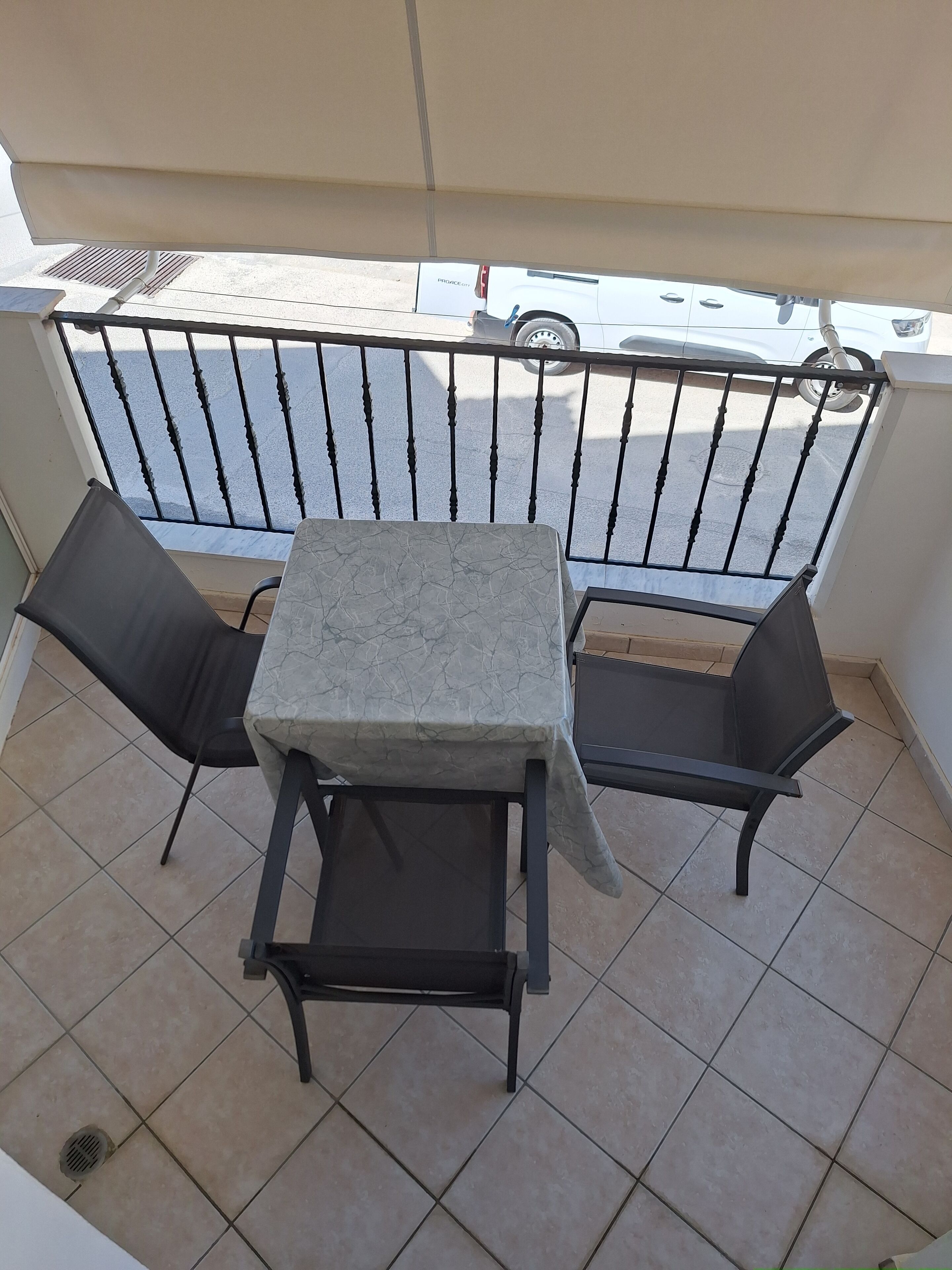 A balcony with a table and two chairs, a metal railing, and a view of the street.