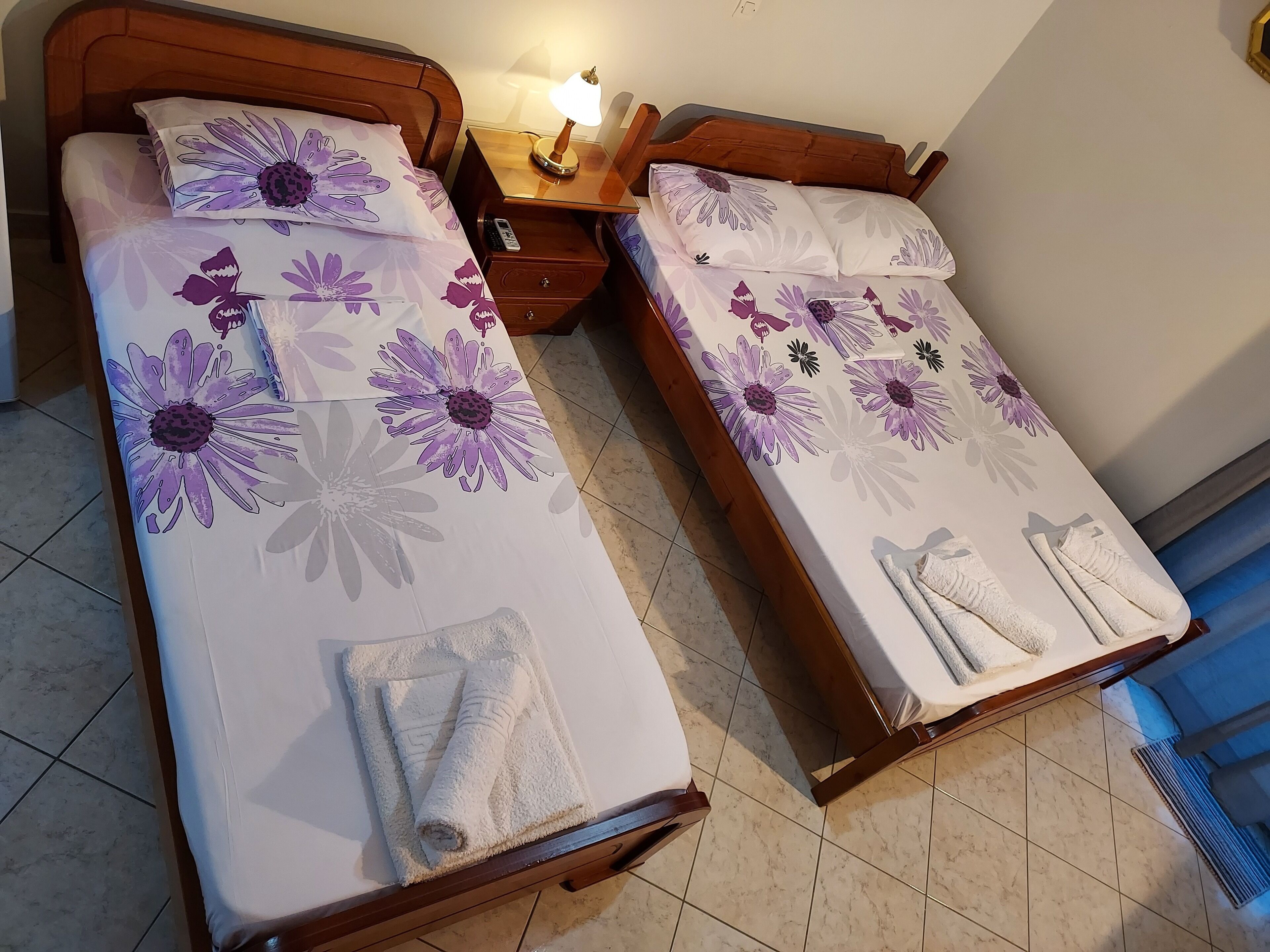 Two single beds with floral bedding, a bedside table with a lamp, and a bathroom with a shower curtain.