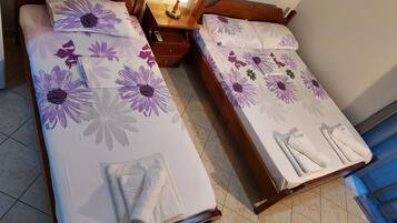 Two single beds with floral bedding, a bedside table with a lamp, and a bathroom with a shower curtain.