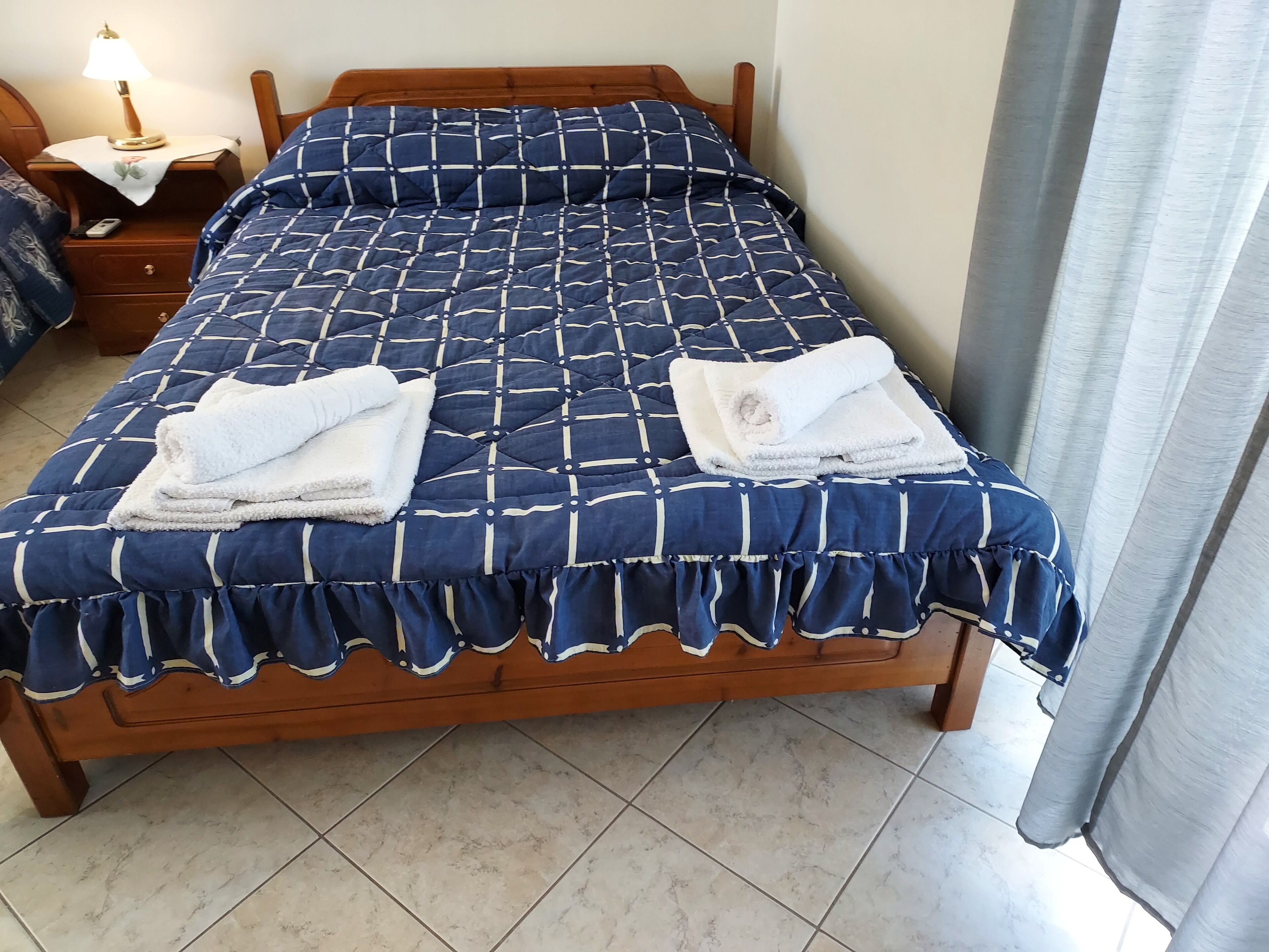 Una cama bien tendida con una colcha azul y blanca estampada y dos toallas blancas dobladas.