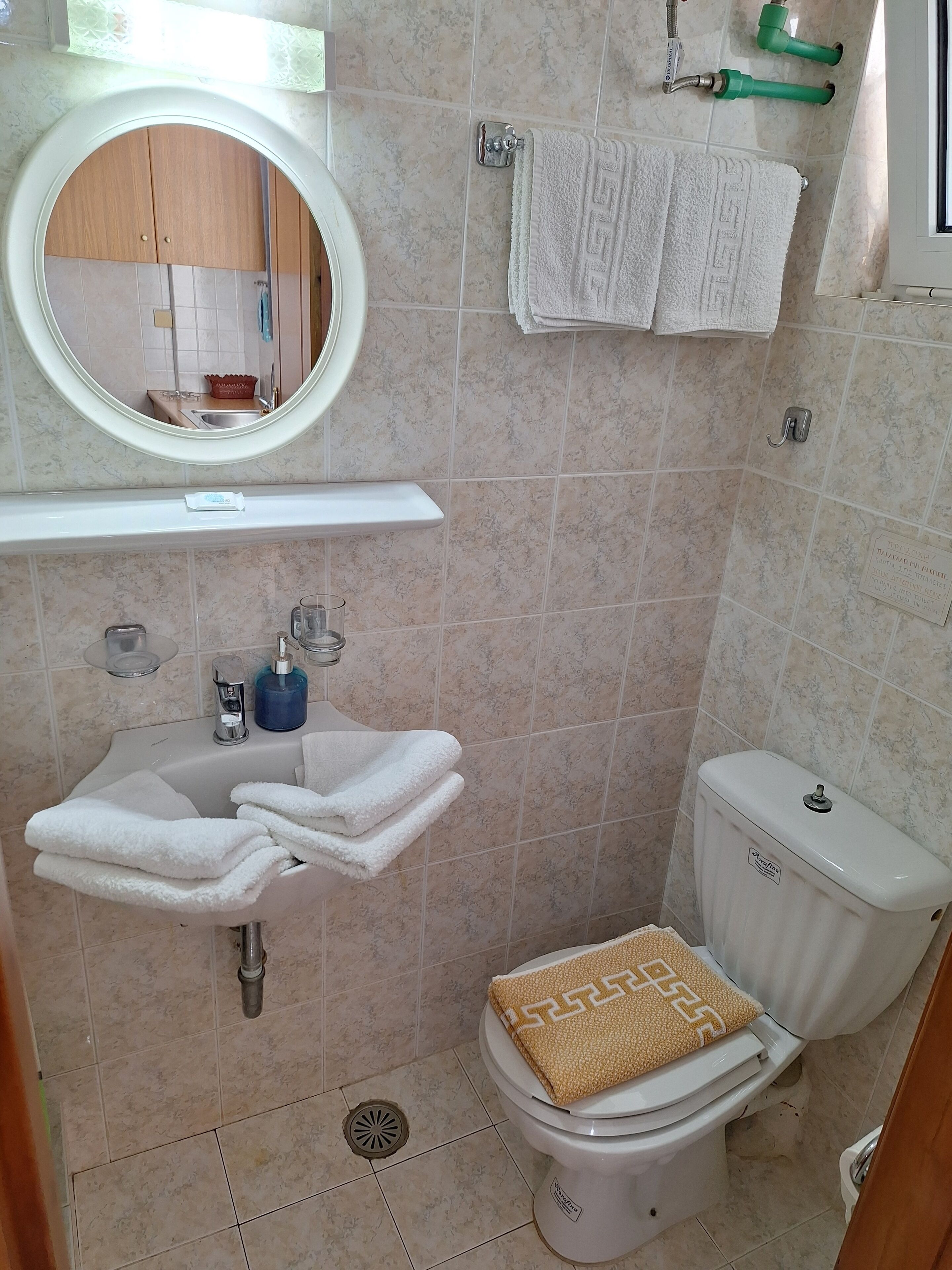 A bathroom with a toilet, sink, and mirror. There are towels and toiletries on the sink.