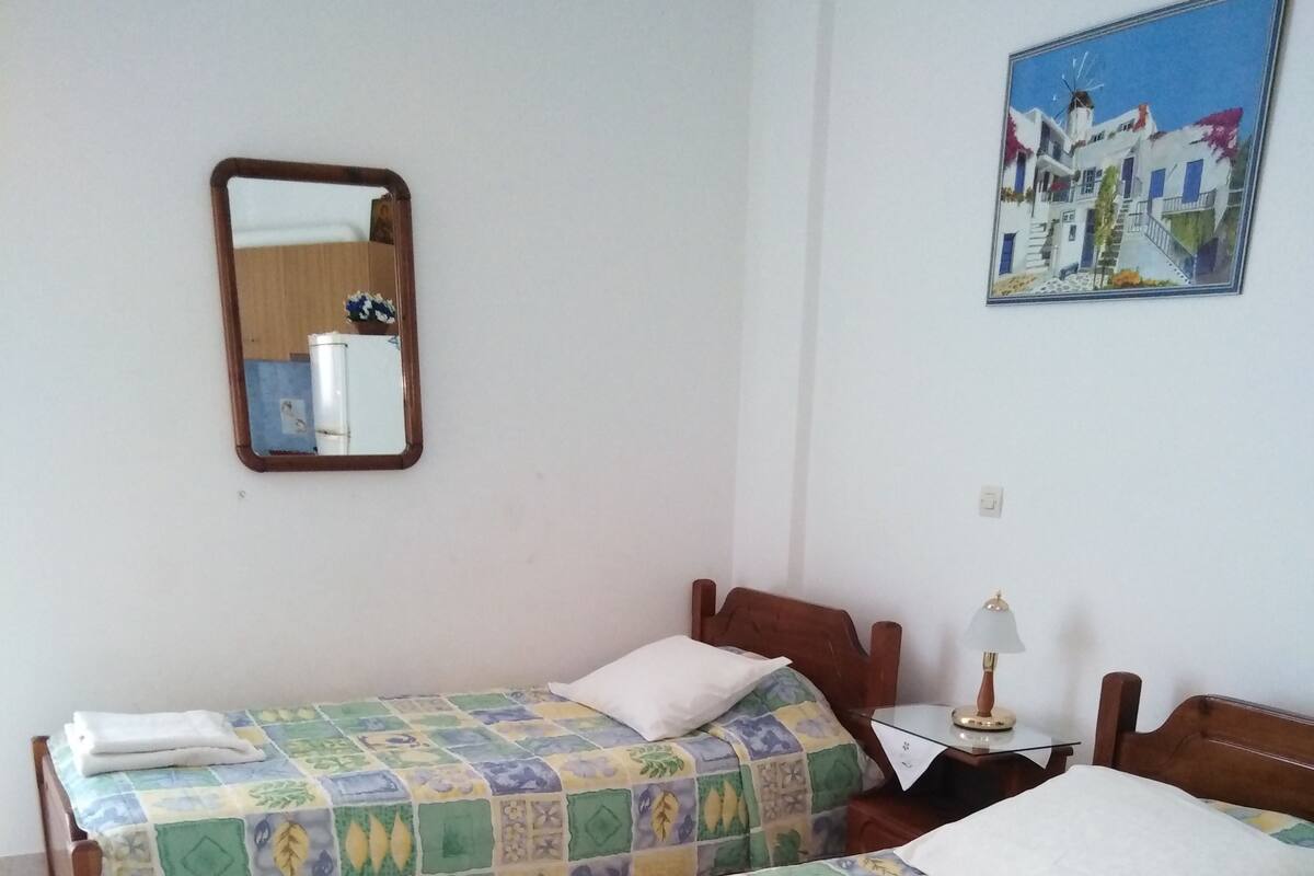 A room with two wooden beds, each with a colorful quilt and white towels. There is a small table with a lamp and a painting on the wall.