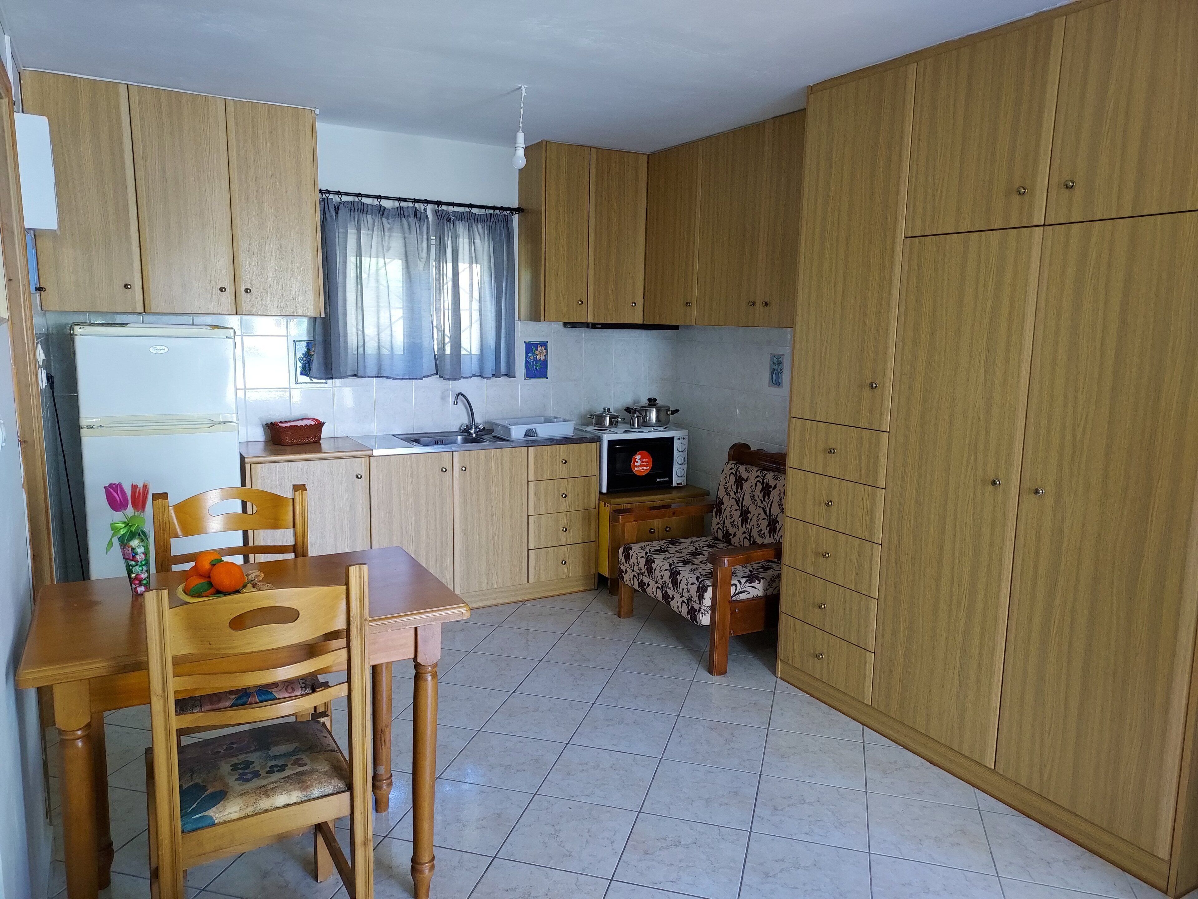 A compact kitchen with wooden cabinets, a refrigerator, a sink, a microwave, and a dining area with a table and chairs.