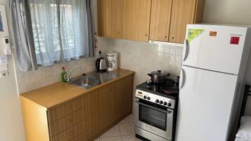 A compact kitchen with wooden cabinets, a stainless steel sink, a coffee maker, an oven, and a refrigerator.