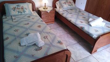 A bedroom with two single beds, each with floral-patterned bedding and a wooden headboard. There is a nightstand with a lamp between the beds, and a wooden dresser to the side.