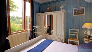 A bedroom with a bed, a wardrobe, a chair, a table with a lamp, and a window with curtains. - Charming Cottage with Terrace and Garden, Pets Welcome (Bussières)