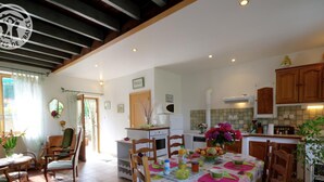 A spacious kitchen with wooden cabinets, a dining area with a table set for four, and a view of the garden through the open door. - Charming Cottage with Terrace and Garden, Pets Welcome (Bussières)