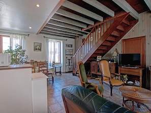 A spacious living area with a wooden staircase, a television, and a dining table. - Charming Cottage with Terrace and Garden, Pets Welcome (Bussières)
