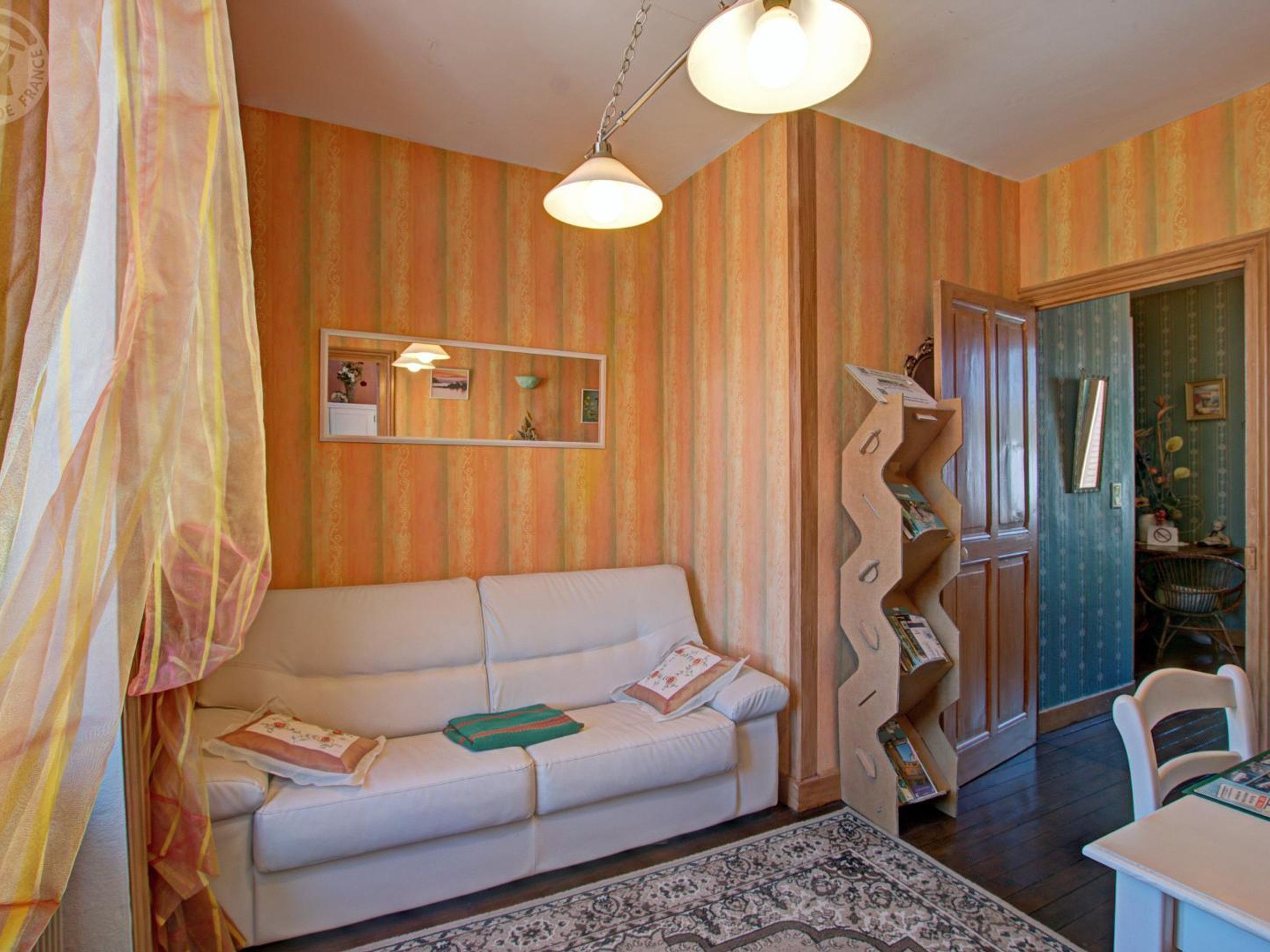 Une pièce avec un canapé blanc, un tapis à motifs, un miroir et une bibliothèque en bois.