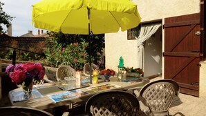 An outdoor dining area with a table set for two, a yellow umbrella, and chairs. - Charming Cottage with Terrace and Garden, Pets Welcome (Bussières)