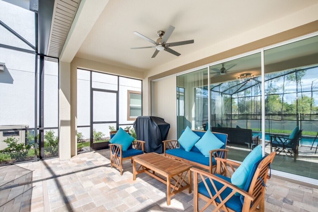 A covered patio with outdoor furniture, a ceiling fan, and large windows offering views of the outdoors.
