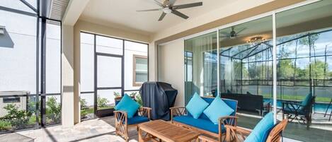 A covered patio with outdoor furniture, a ceiling fan, and large windows offering views of the outdoors.