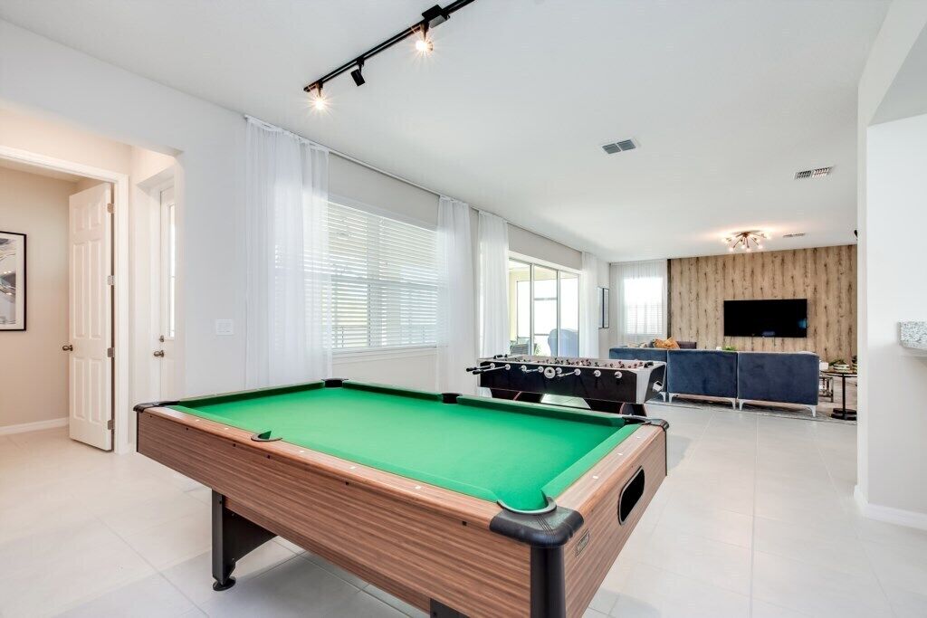 Une table de billard dans un salon moderne, avec un canapé et un téléviseur.