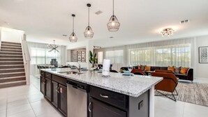 Una cocina moderna con encimeras de granito, lavavajillas y una isla grande. Hay una zona de comedor con sofá y mesa de centro.