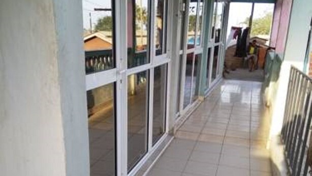 A covered corridor with tiled flooring, large glass doors leading outside, and a white bucket on the floor. - Shiloh Accommodation (Mombasa)