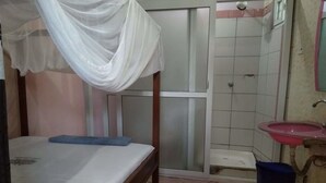 A bedroom with a bed, a white canopy, a bathroom with a sink and mirror, and a shower area. - Shiloh Accommodation (Mombasa)