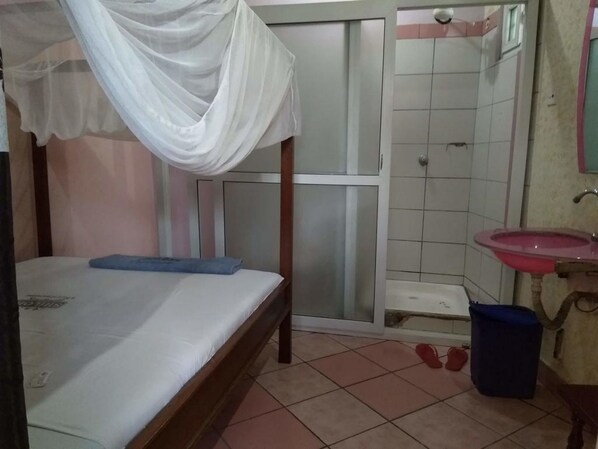 A bedroom with a bed, a white canopy, a bathroom with a sink and mirror, and a shower area. - Shiloh Accommodation (Mombasa)