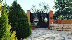 A stone-paved courtyard with a gated entrance, surrounded by greenery and a stone wall. - L'Eremo Luxury Apartments (Corfu)