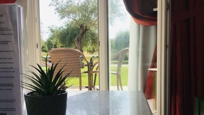 A view through a window with a potted plant on a table, a wicker chair, and a red curtain. - L'Eremo Luxury Apartments (Corfu)