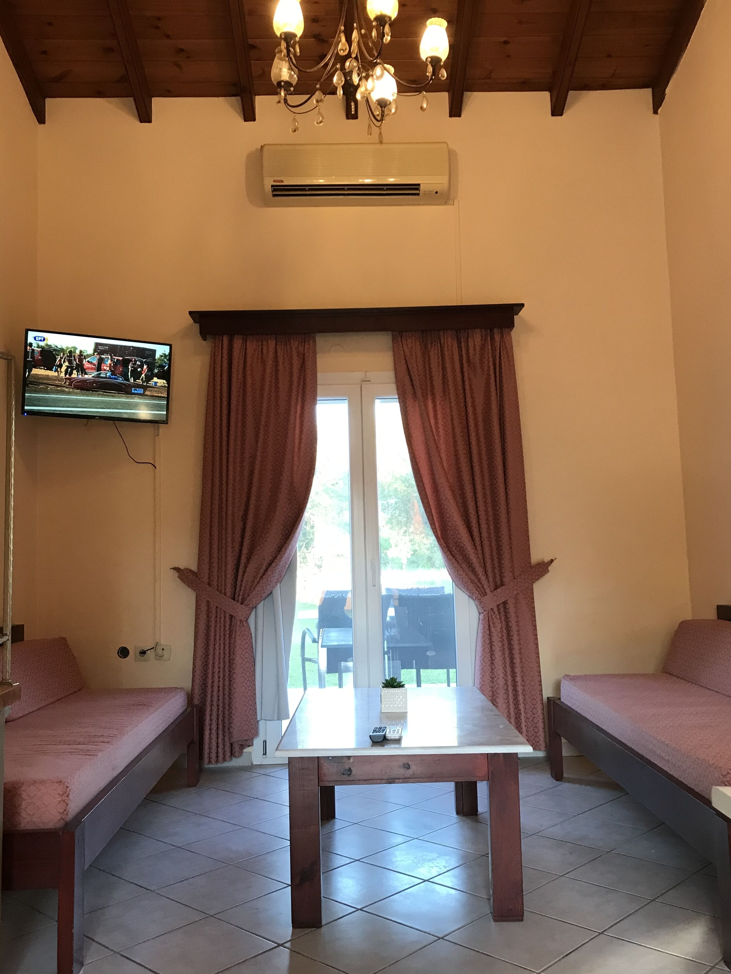A room with two pink beds, a wooden table, a TV mounted on the wall, and a ceiling fan.