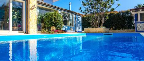 A modern house with a swimming pool, stone pillars, and tropical plants.