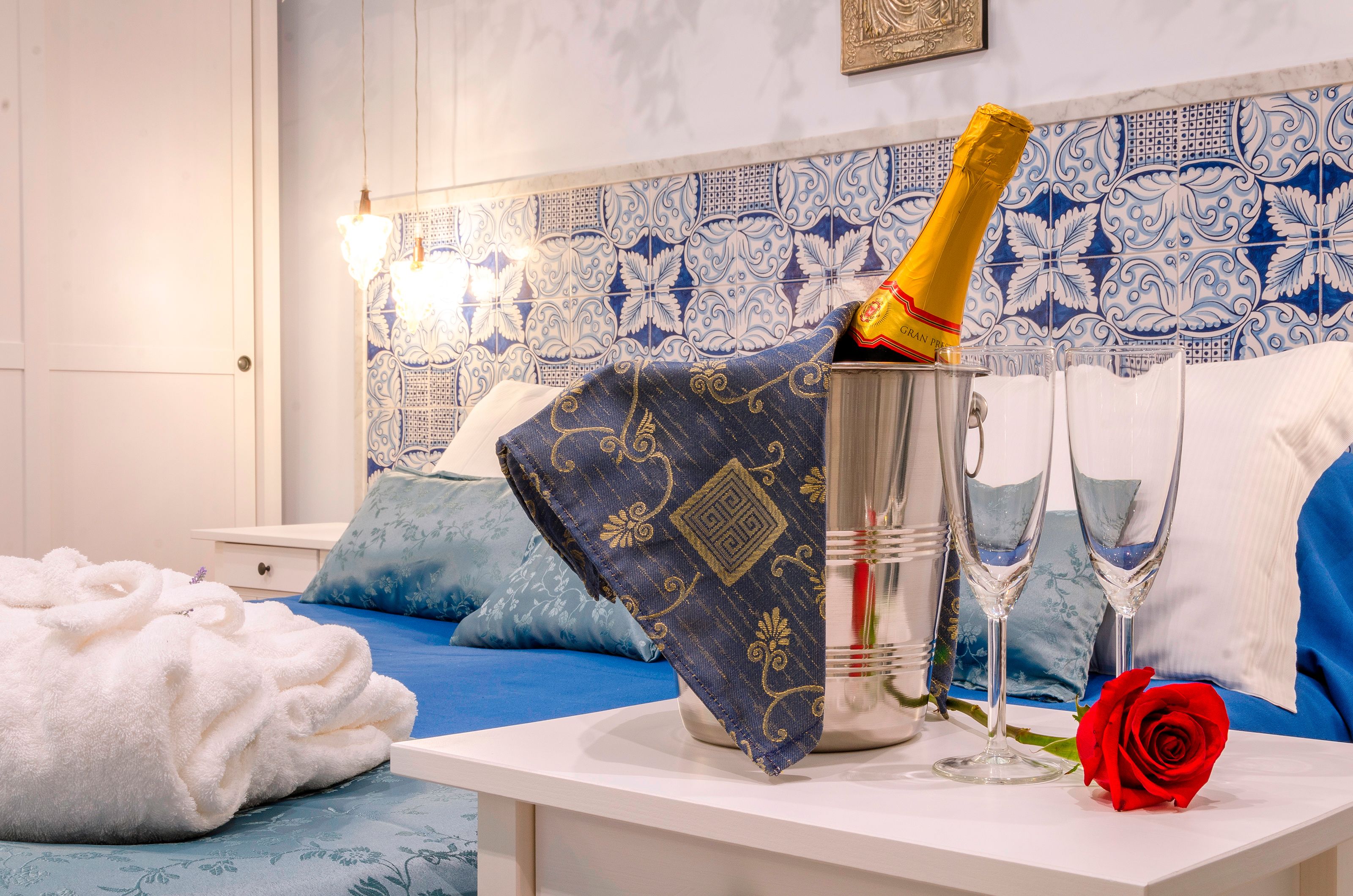 Una habitación con una cama, una mesita de noche con una botella de champán, dos copas y una rosa roja.