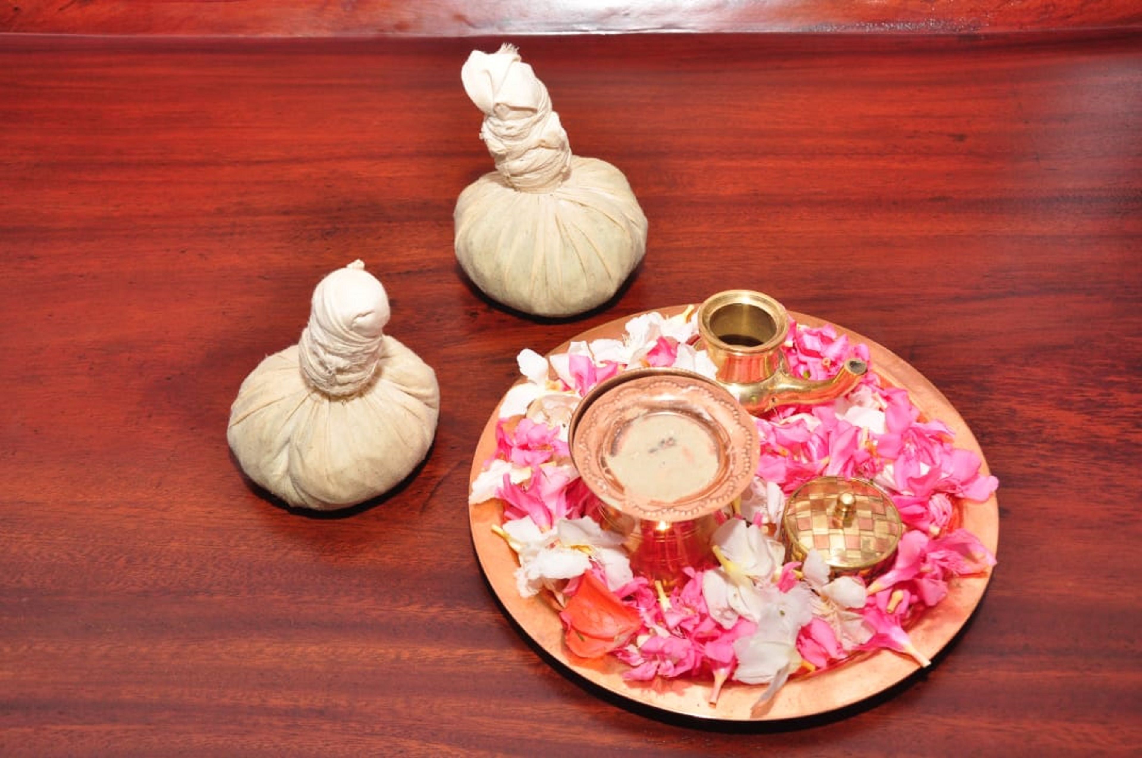 A wooden tray with three white objects and a glass container surrounded by pink and white flower petals.