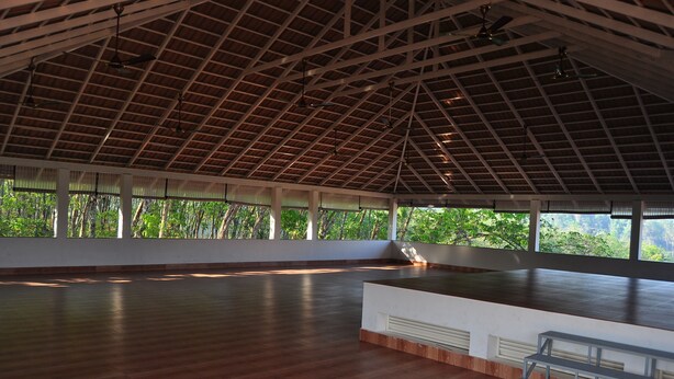 An indoor space with a high ceiling, large windows, and a wooden floor. - INDIMASI - Ayurveda & Healing Village (Nedumangad)