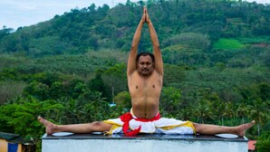 A man performing a yoga pose on a rooftop with a lush green landscape in the background. - INDIMASI - Ayurveda & Healing Village (Nedumangad)