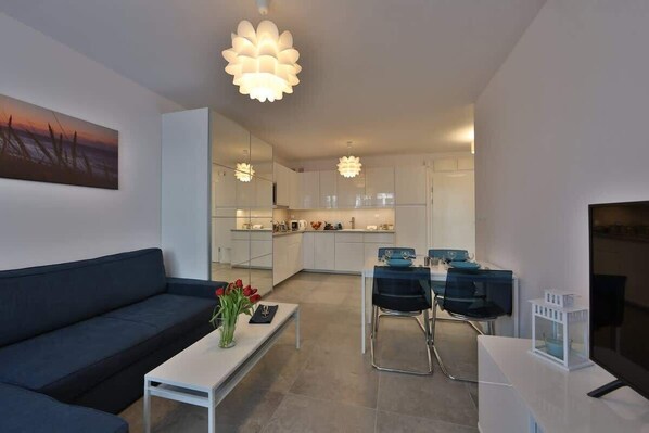 A modern living room with a sofa, coffee table, and a dining area with chairs and a table.