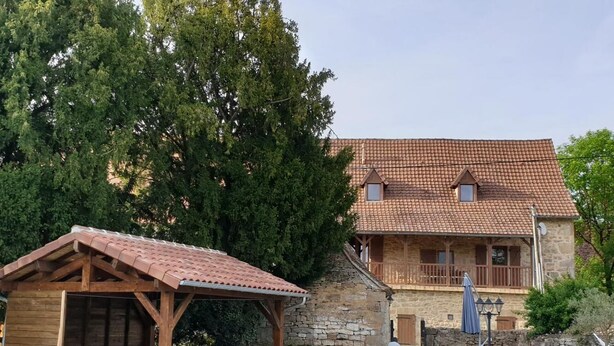 A stone building with a tiled roof, a wooden pergola, and a swimming pool. - Gîte Le Chant des Ifs (Bio)