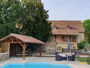 Un edifici de pedra amb teulada de rajola, una pèrgola de fusta i una piscina.
