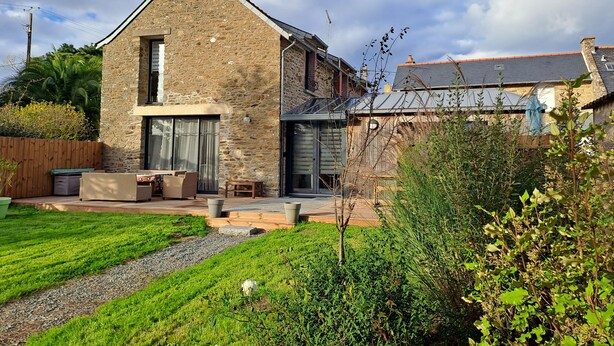 A stone house with a large patio, a wooden fence, and a garden.