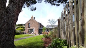 A stone house with a garden, a wooden fence, and a large tree.