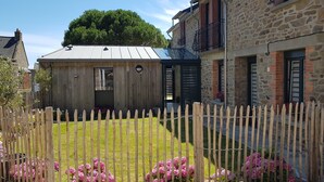 A wooden house with a metal roof, a stone building with a balcony, and a wooden fence with pink flowers.