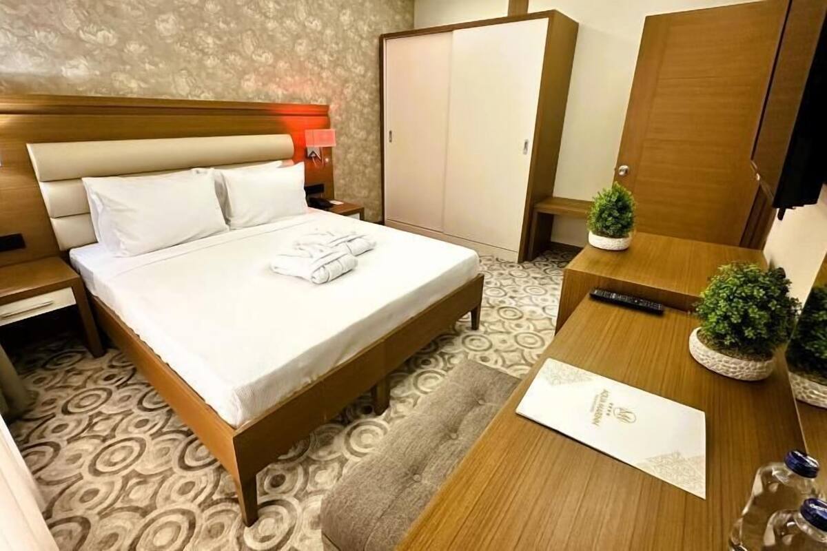 A neatly arranged hotel room with a bed, a nightstand, a wardrobe, and a small table with a plant.