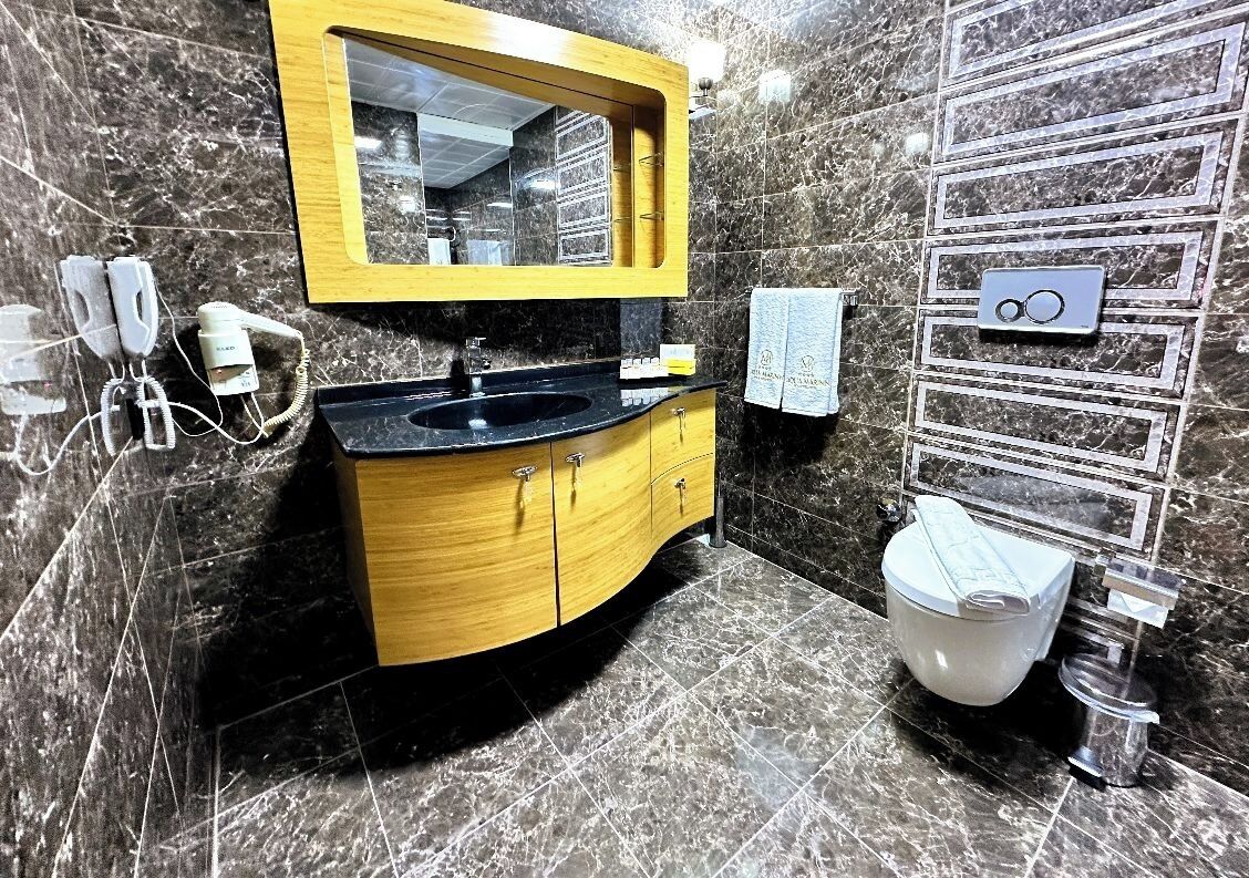 A bathroom with a marble sink, wooden vanity, and a toilet.