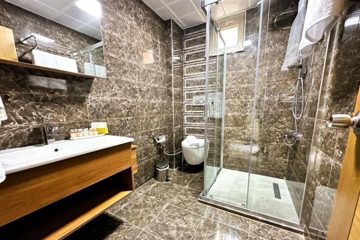 A bathroom with a glass-enclosed shower, marble walls, and a wooden vanity.