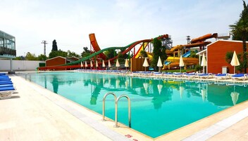 Una piscina con toboganes acuáticos cercanos, sillas de descanso y sombrillas.