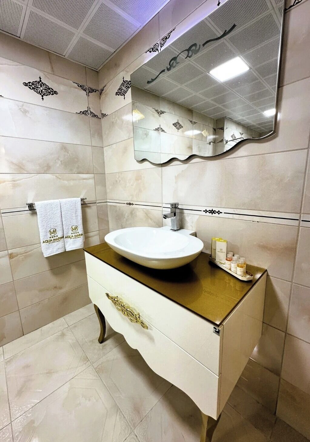 Un baño con un lavabo blanco, una tocador con encimera dorada y un espejo grande.