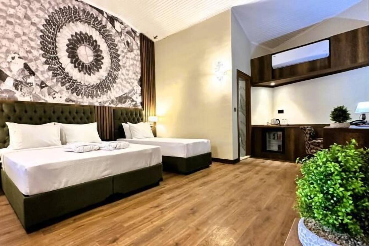 A hotel room with a large bed, a smaller bed, a desk, and a potted plant.