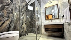 A bathroom with a marble wall, a glass shower enclosure, a white toilet, a sink with a wooden vanity, and a mirror above the sink. - Aqua Marin Spa&Wellness (Altinova)