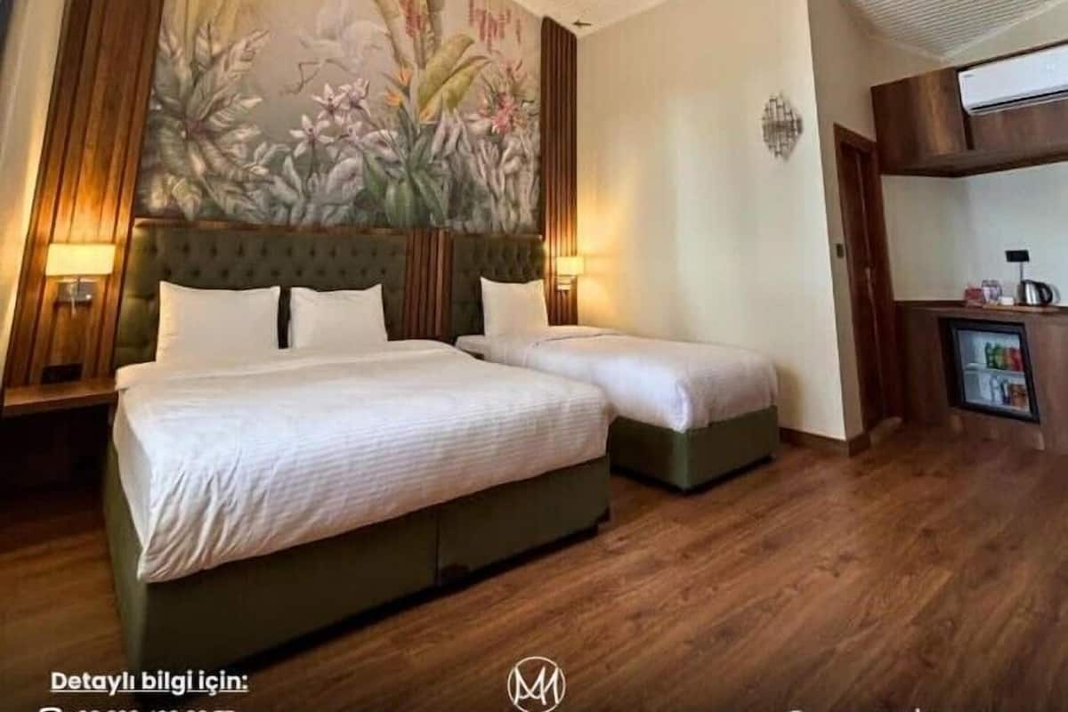 A hotel room with two beds, a large floral mural on the wall, wooden flooring, and a small kitchenette.