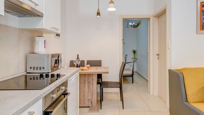Una cucina compatta con elettrodomestici moderni, un'area pranzo con tavolo in legno e un divano giallo.