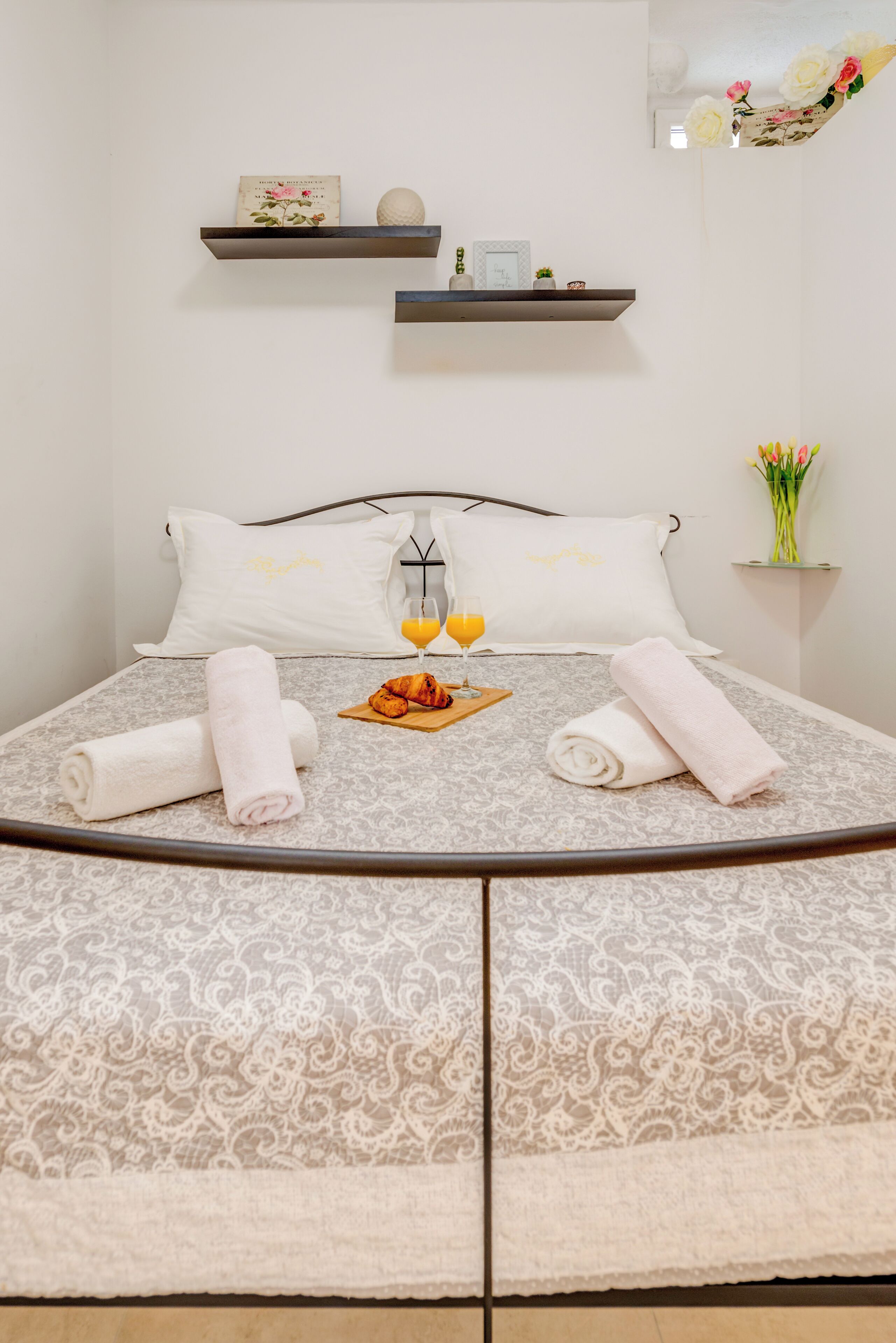 Cama bem arrumada com colcha estampada, dois toalhas enroladas, bandeja com croissants e suco de laranja, e um copo de suco de laranja.