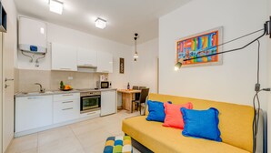 Una cucina moderna con mobili bianchi, un'area pranzo con tavolo e sedie, e un divano giallo con cuscini colorati.