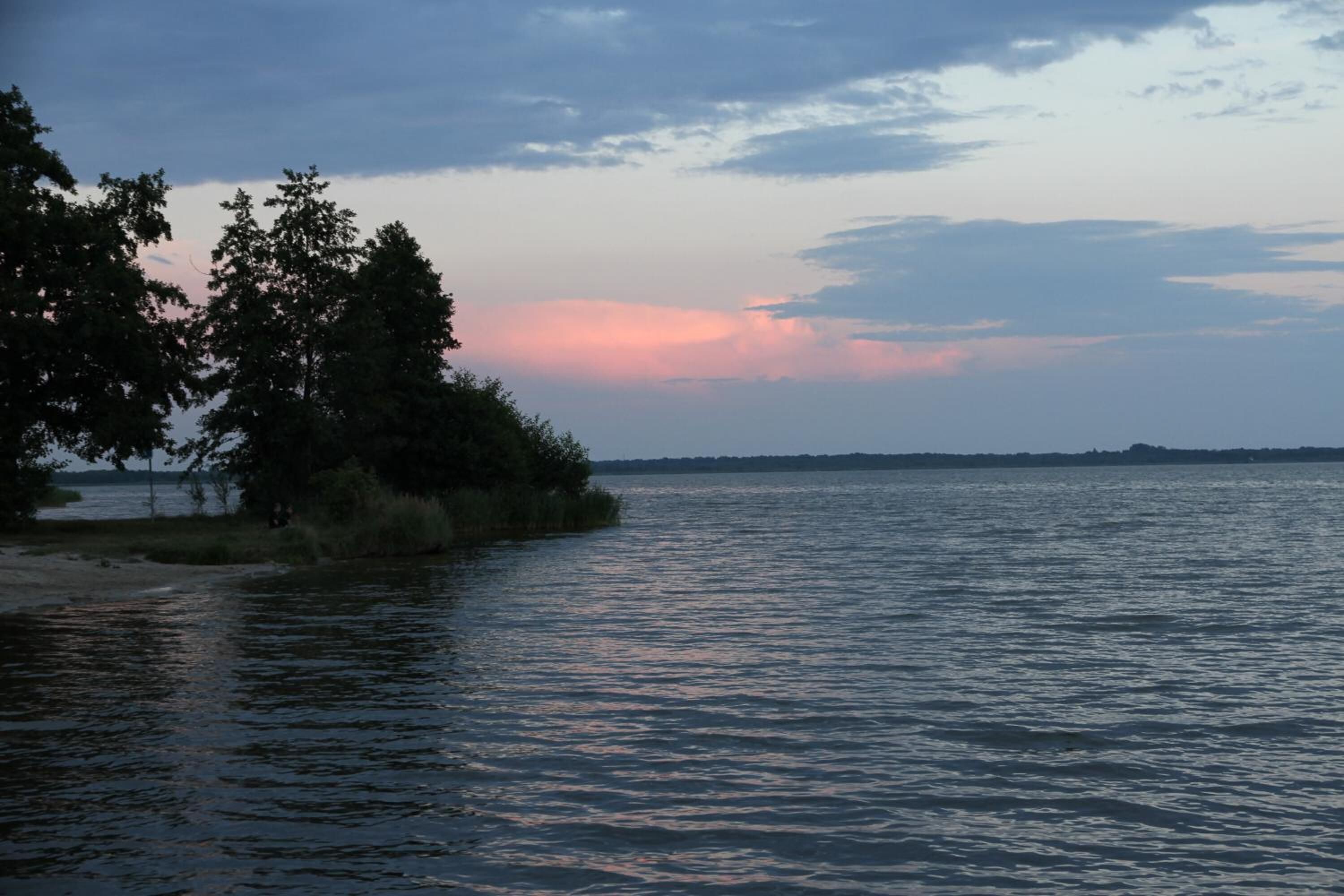 A calm lake with trees on the left and a clear sky.