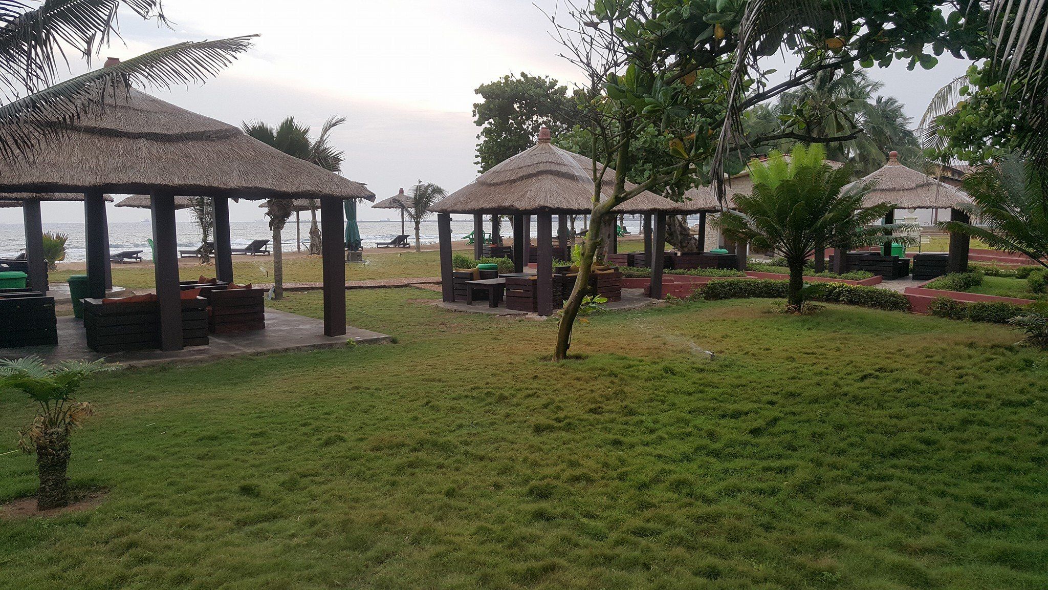 A beachside resort with thatched-roof gazebos, outdoor seating, and a view of the ocean.